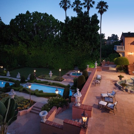 The terrace of the Hearst Estate at sunset featuring a fountain, multiple pools and lush greenery with palm trees in the background against a blue sky
