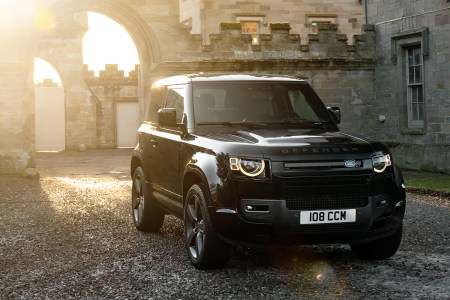 A V8 Carpathian Edition Land Rover Defender SUV in black sitting in the courtyard of a castle in the UK while the sun sets in the background behind the stone walls