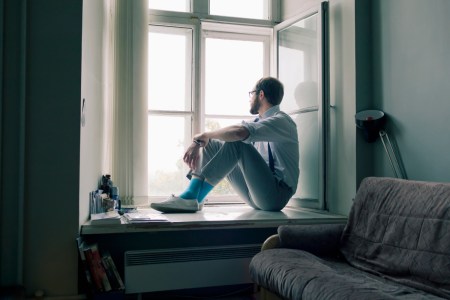 Lonely man sits on window sill gazing out the window