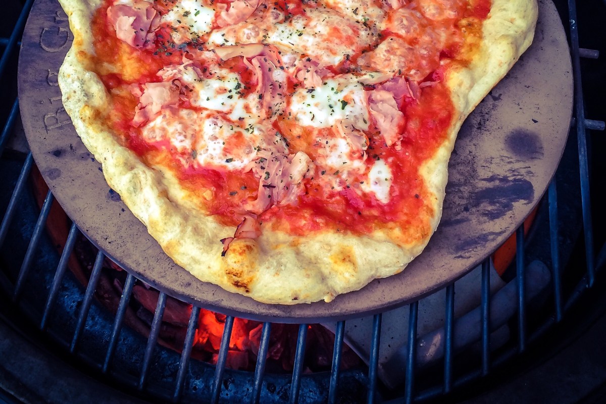 a prosciutto pizza cooks on a charcoal grill