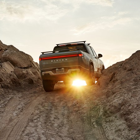 The Rivian R1T electric pickup truck shown from the rear driving over a rocky dirt hill at sunset