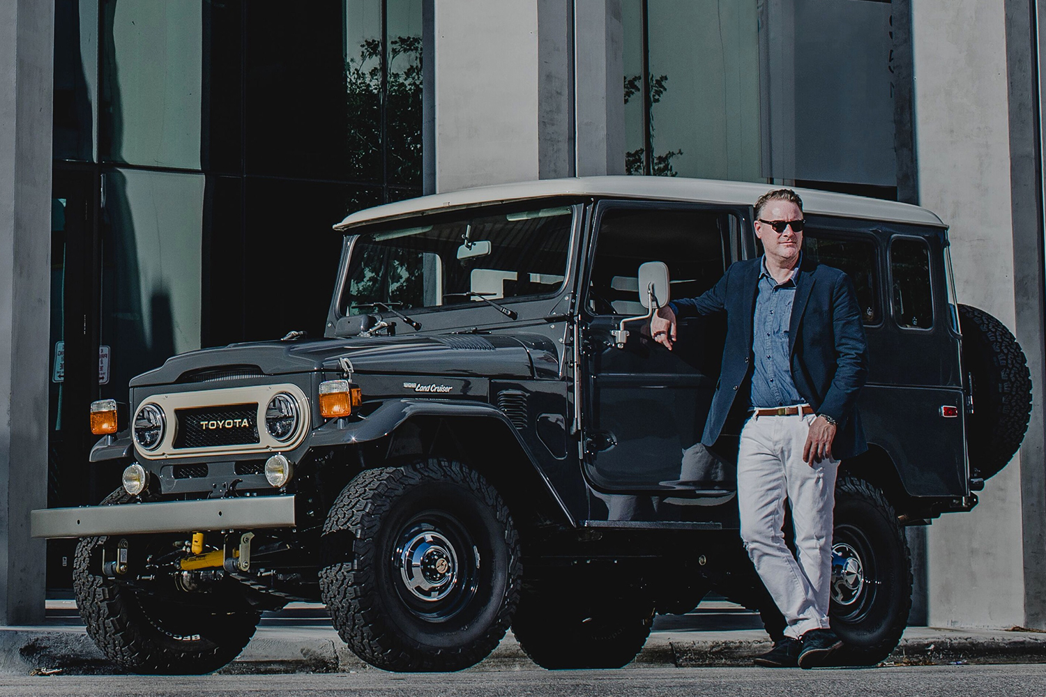 Menswear designer Todd Snyder in white pants and a blue jacket standing next to a custom Toyota Land Cruise designed in partnership with The FJ Company