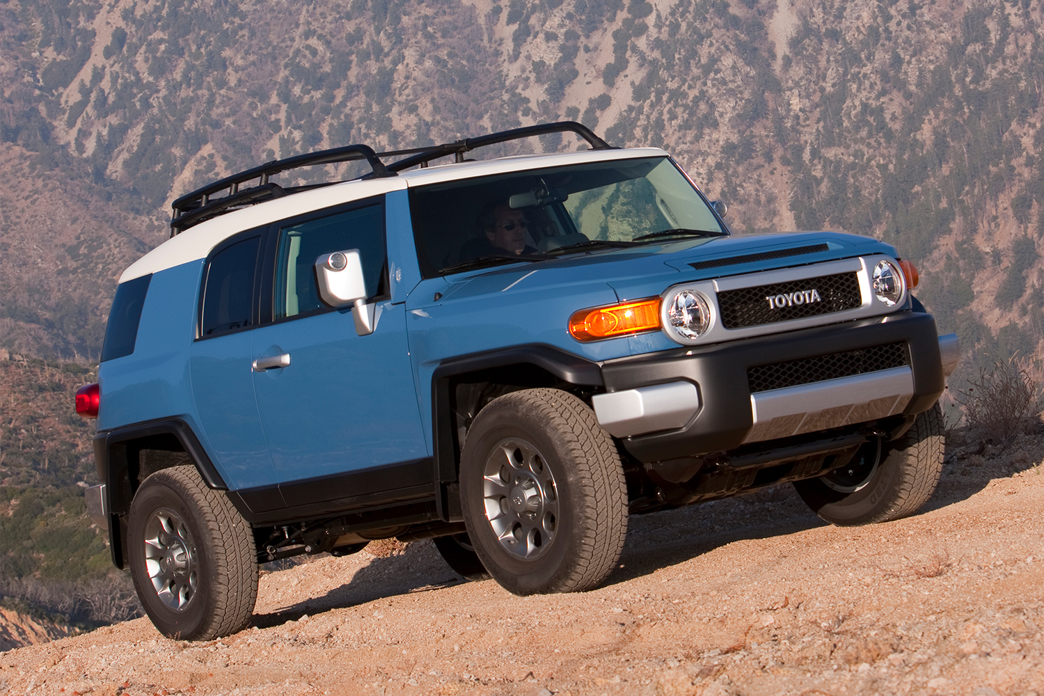 A blue Toyota FJ Cruiser driving up a rock face. The vintage off-road SUV is increasing in value in 2021, seven years after it was discontinued.