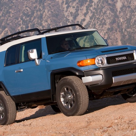 A blue Toyota FJ Cruiser driving up a rock face. The vintage off-road SUV is increasing in value in 2021, seven years after it was discontinued.
