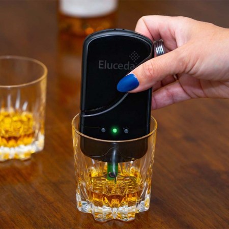 Eluceda's handheld device, the E-Sens, being placed by hand in a glass of whisky. The device reportedly can identify counterfeit whisky.