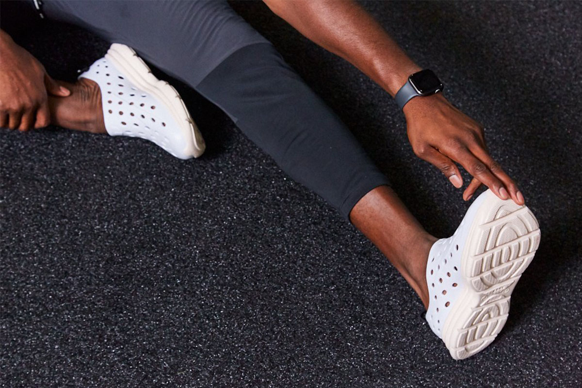 A man wearing recovery footwear stretches on a mat.