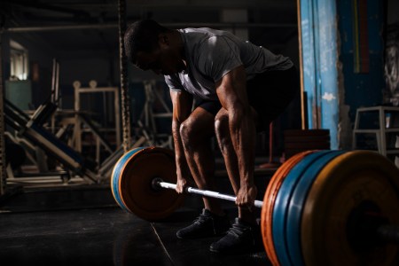 A man lifting a heavy barbell in a darkly lit gym.
