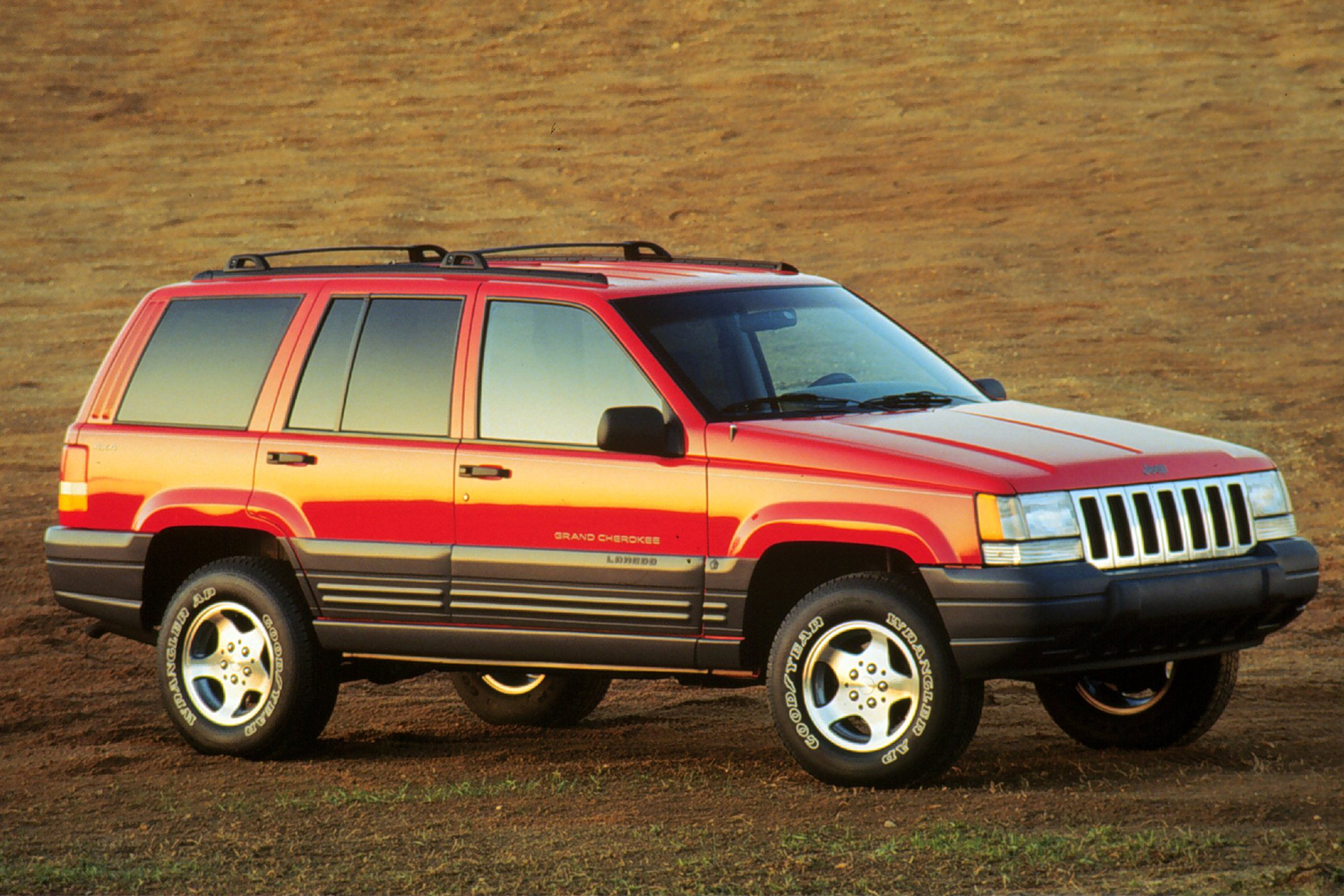 A 1996 Jeep Grand Cherokee Laredo in red sitting on the dirt in a vintage photo