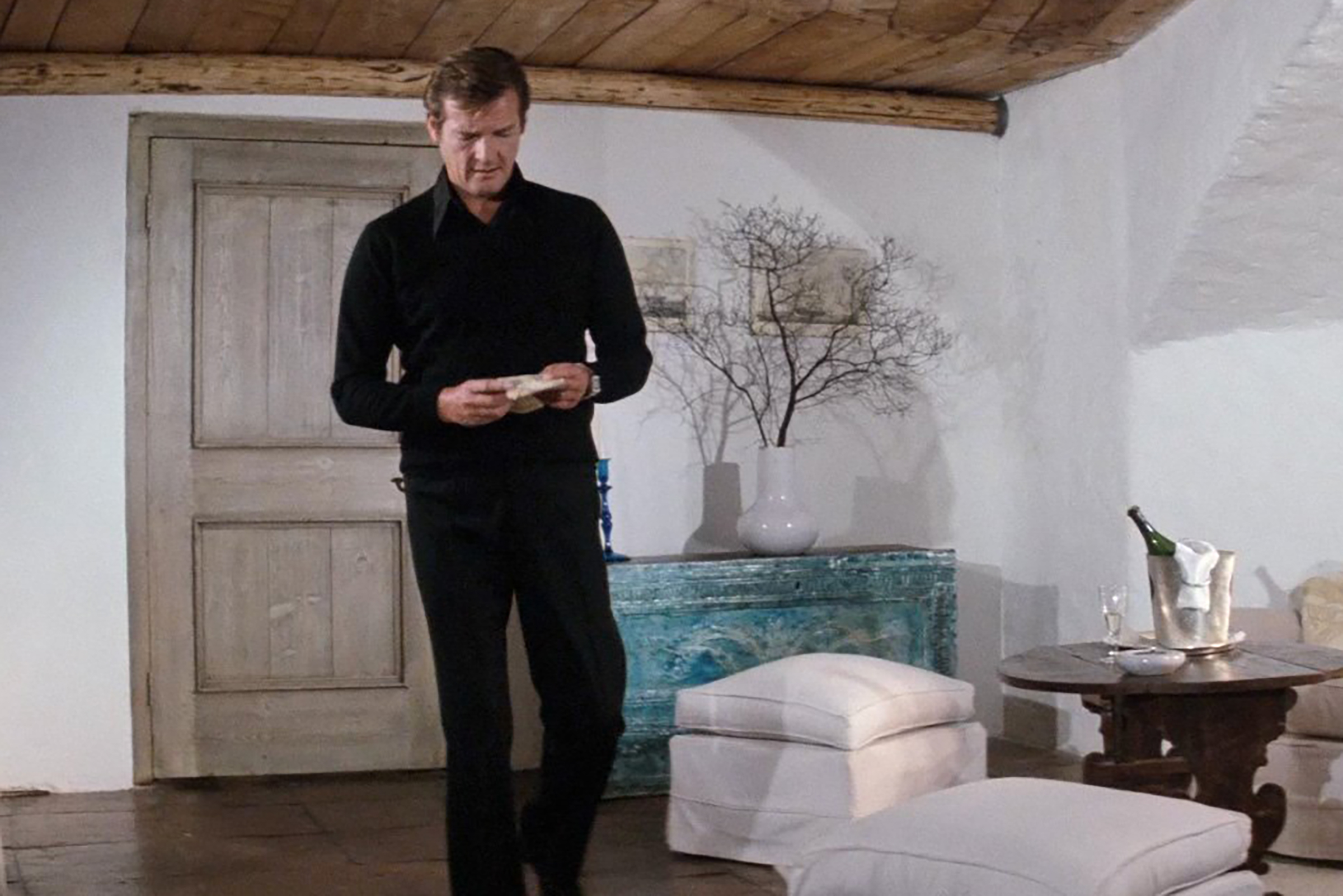 Moore sports black trousers and a black button down layered under a black v-neck sweater in The Spy Who Loved Me.