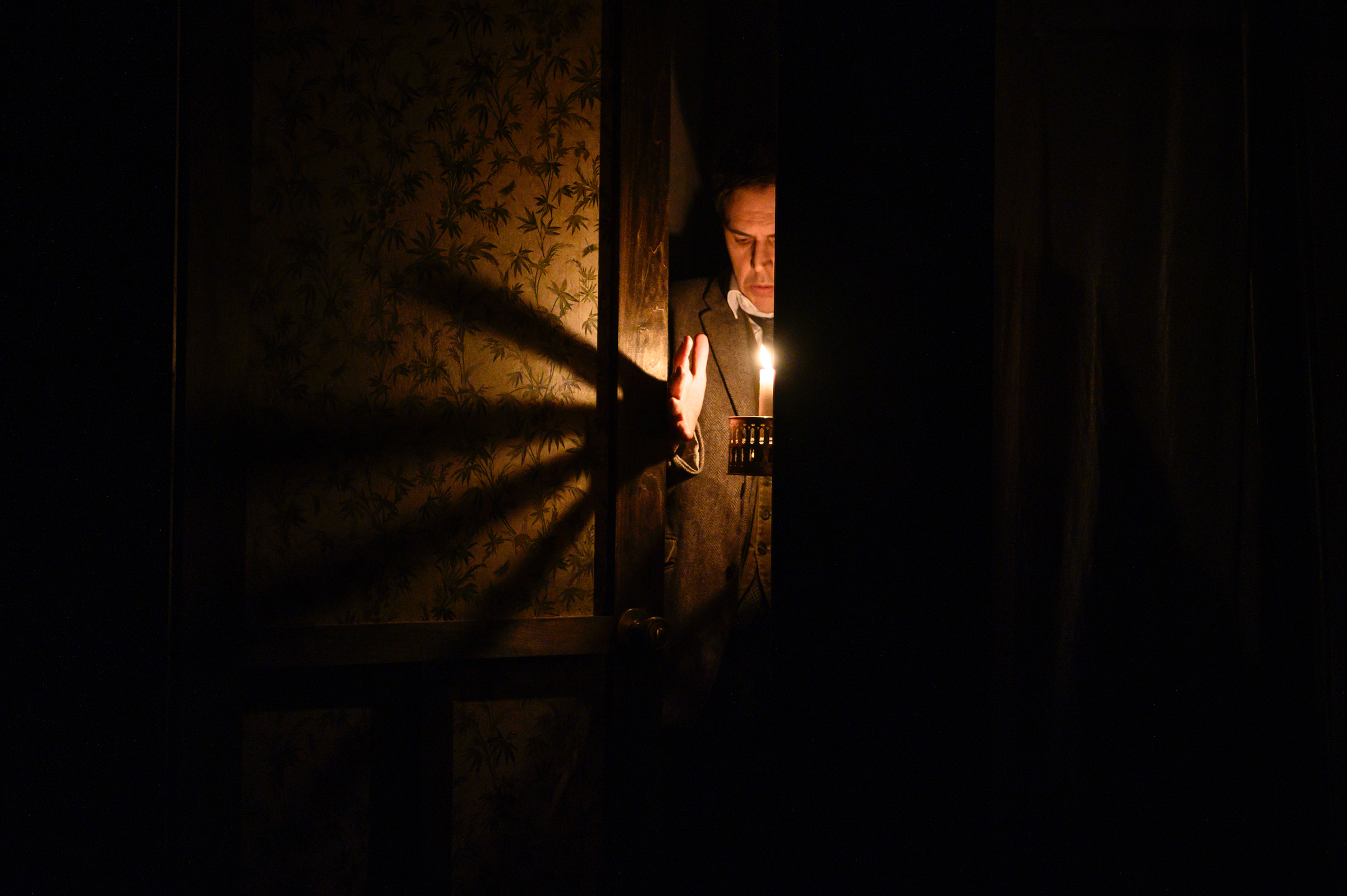 Ben Porter holds a candle and casts a shadow of his hand across the wall in "The Woman in Black" at the McKittrick Hotel.