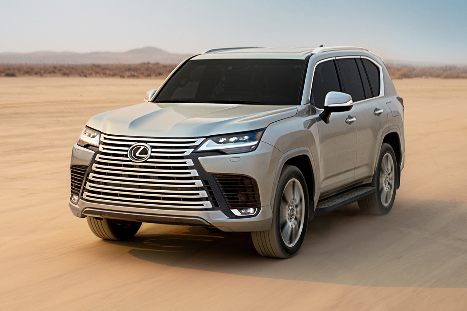 The 2022 Lexus LX 600 SUV with a large front grille driving through the desert on sand during the day