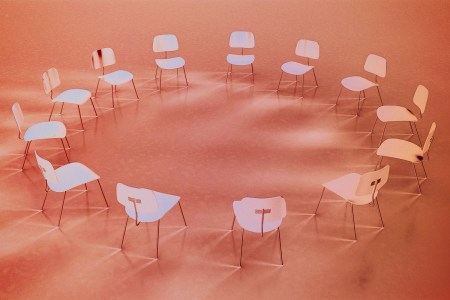 A circle of empty chairs against a light red background.