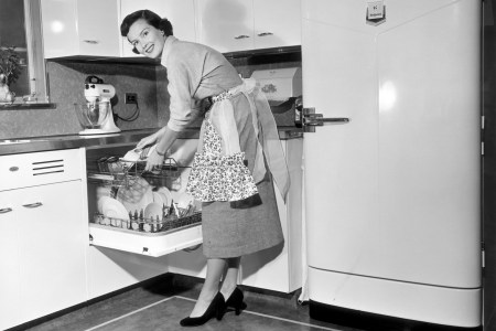 A 1950s housewife stands at the dishwasher in the kitchen.