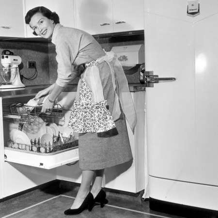 A 1950s housewife stands at the dishwasher in the kitchen.