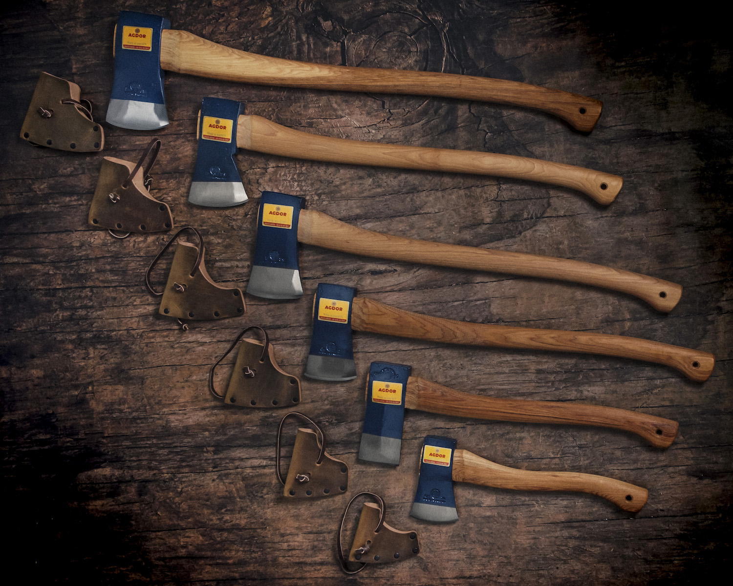 The six Agdor axes from Hults Bruk that are now on sale in the U.S. as of 2021 with their leather sheaths lying on a wood table