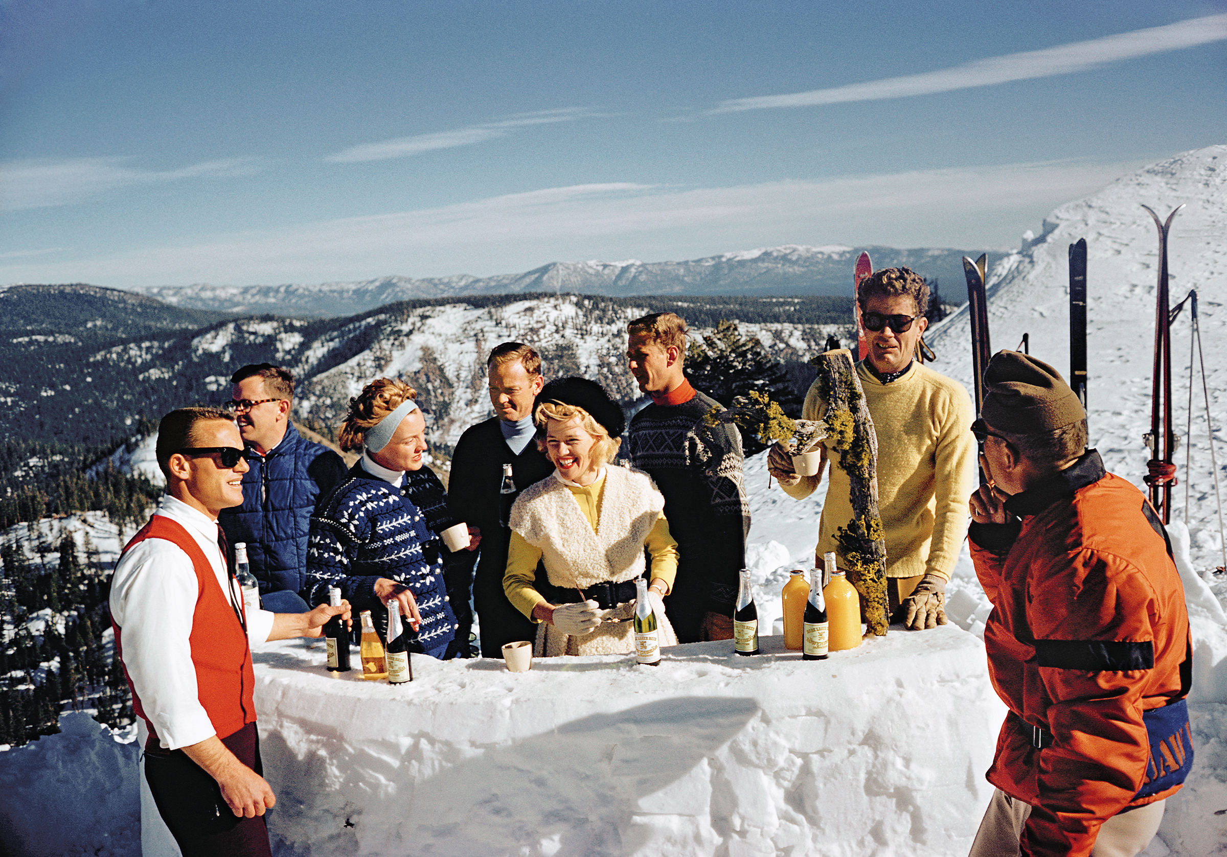 Skiers celebrating with a little après-ski atop a snowy mountain, captured by photographer Slim Aarons.