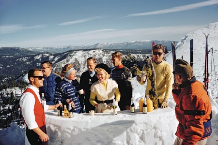 Skiers celebrating with a little après-ski atop a snowy mountain, captured by photographer Slim Aarons.