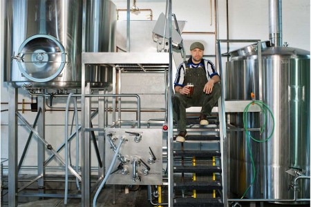 Man sitting in a brewery drinking a beer on some steps. A new survey by the Brewers Association suggests most U.S. brewery owners are white and male.