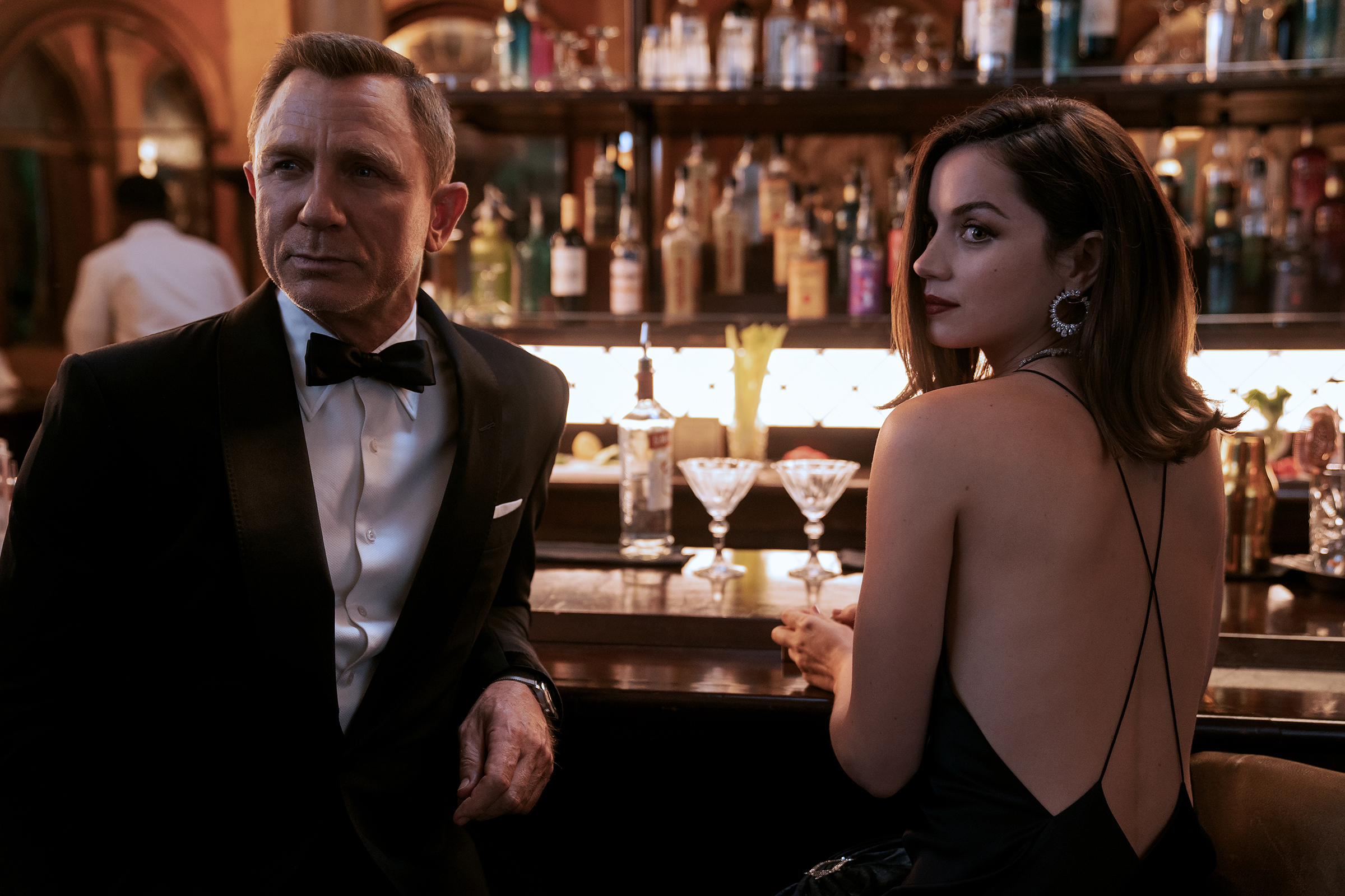 James Bond (Daniel Craig) and Paloma (Ana de Armas) sit at a bar in NO TIME TO DIE, an EON Productions and Metro-Goldwyn-Mayer Studios film