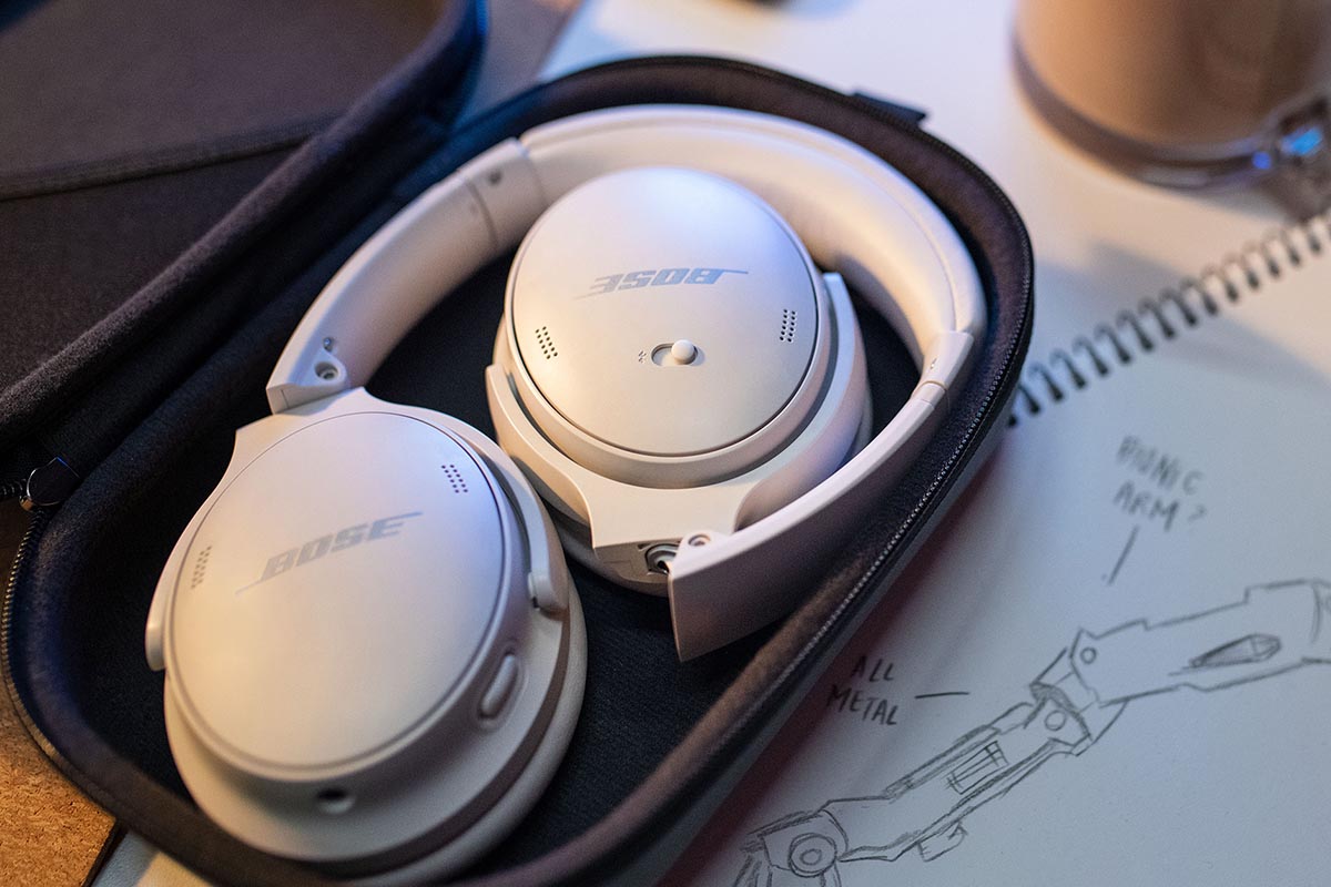 A pair of smoke white Bose QuietComfort 45 headphones lying in their case on a desk. The new headphones offer excellent noise cancellation.