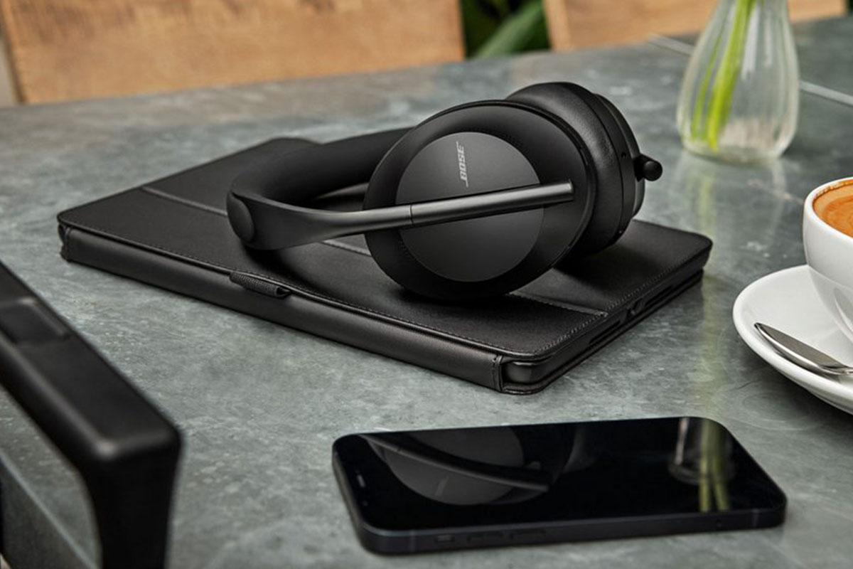 A pair of black Bose 700 headphones lying on a desk near a smartphone