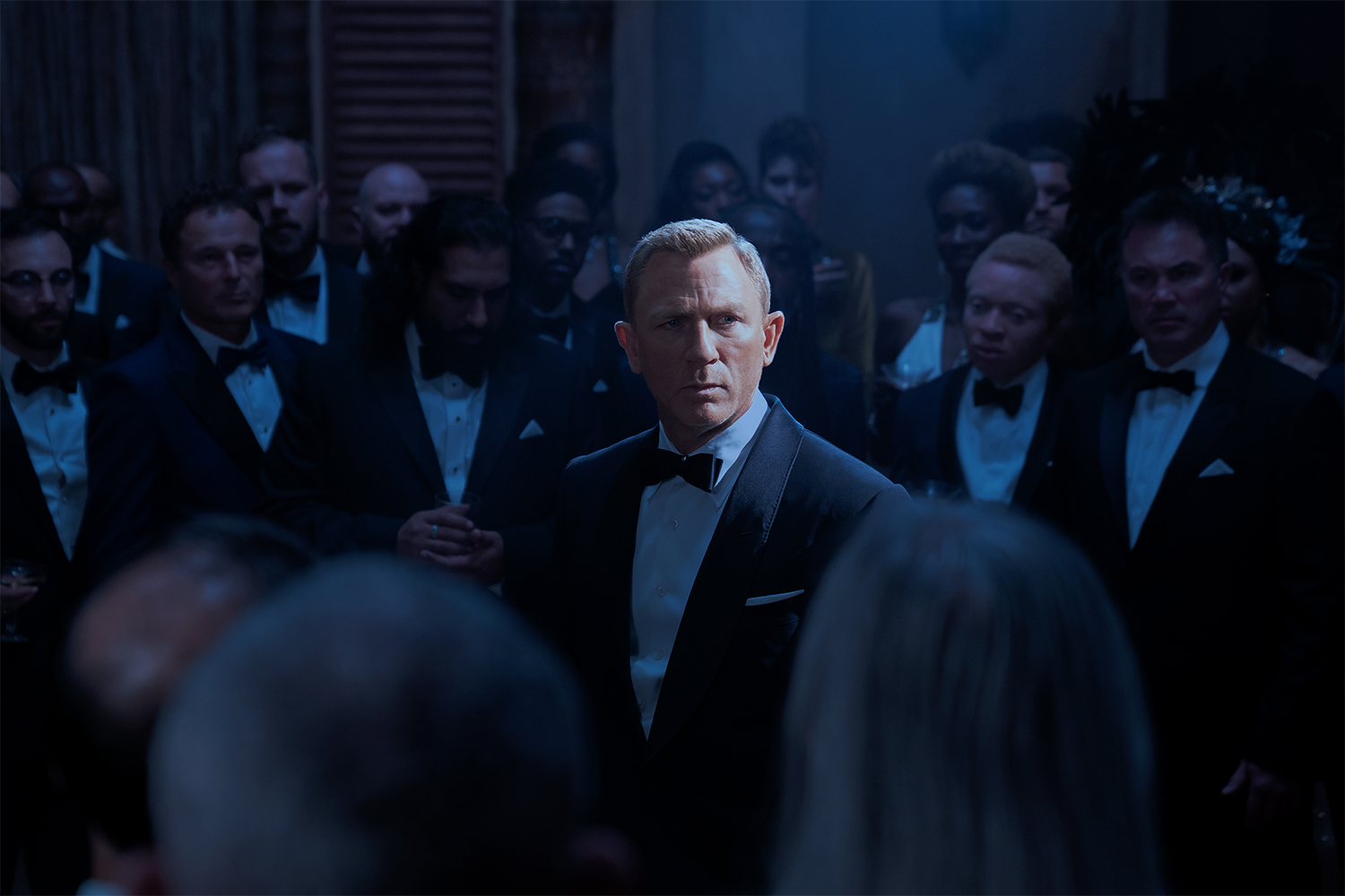 Daniel Craig as James Bond pictured in a tuxedo in "No Time to Die," surrounded by enemies from the secret organization Spectre