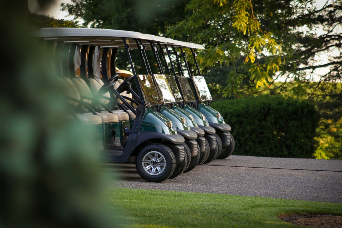 A line of green and tan golf carts sitting on a golf course in the early morning light