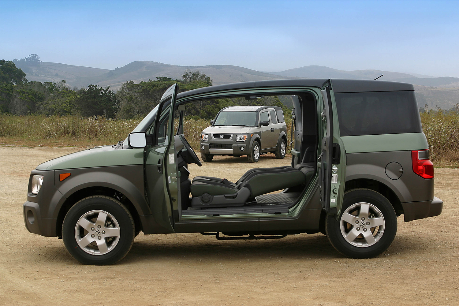 A Honda Element with the doors open showing folded down seats and another Element SUV in the background on the beach