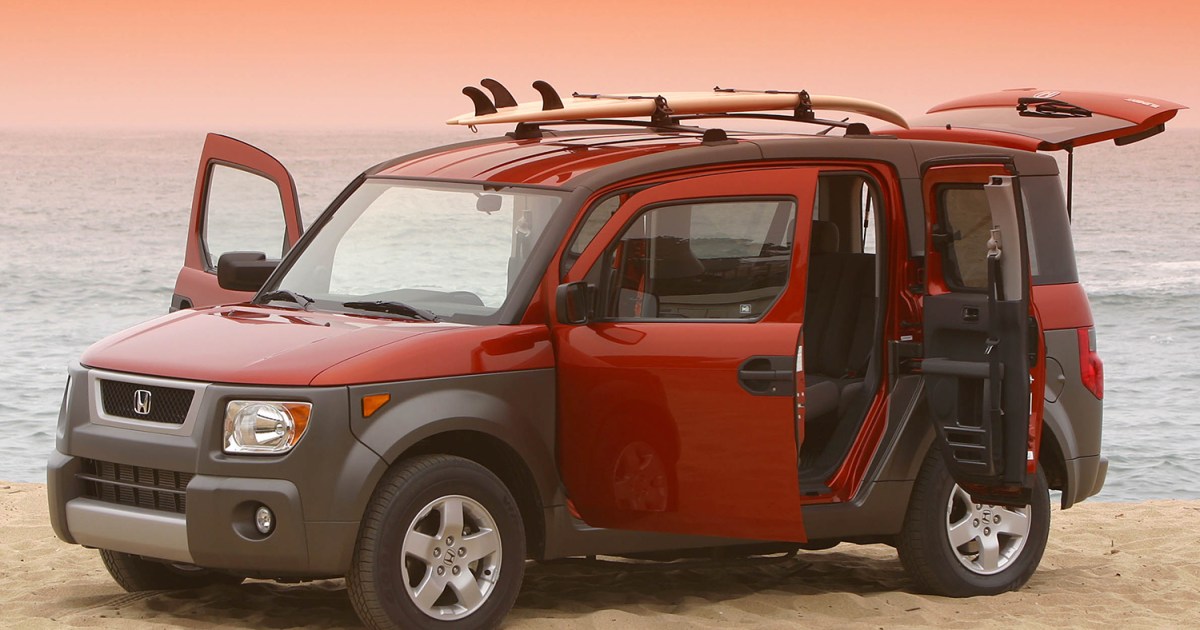 An orange and brown Honda Element with all the doors open and a surfboard on top sitting on the beach at sunset