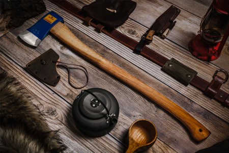 The Agdor 32 Yankee Felling Axe from Hults Bruk, available in the U.S. as of July 2021, lying on a wood table next to a leather sheath and other tools