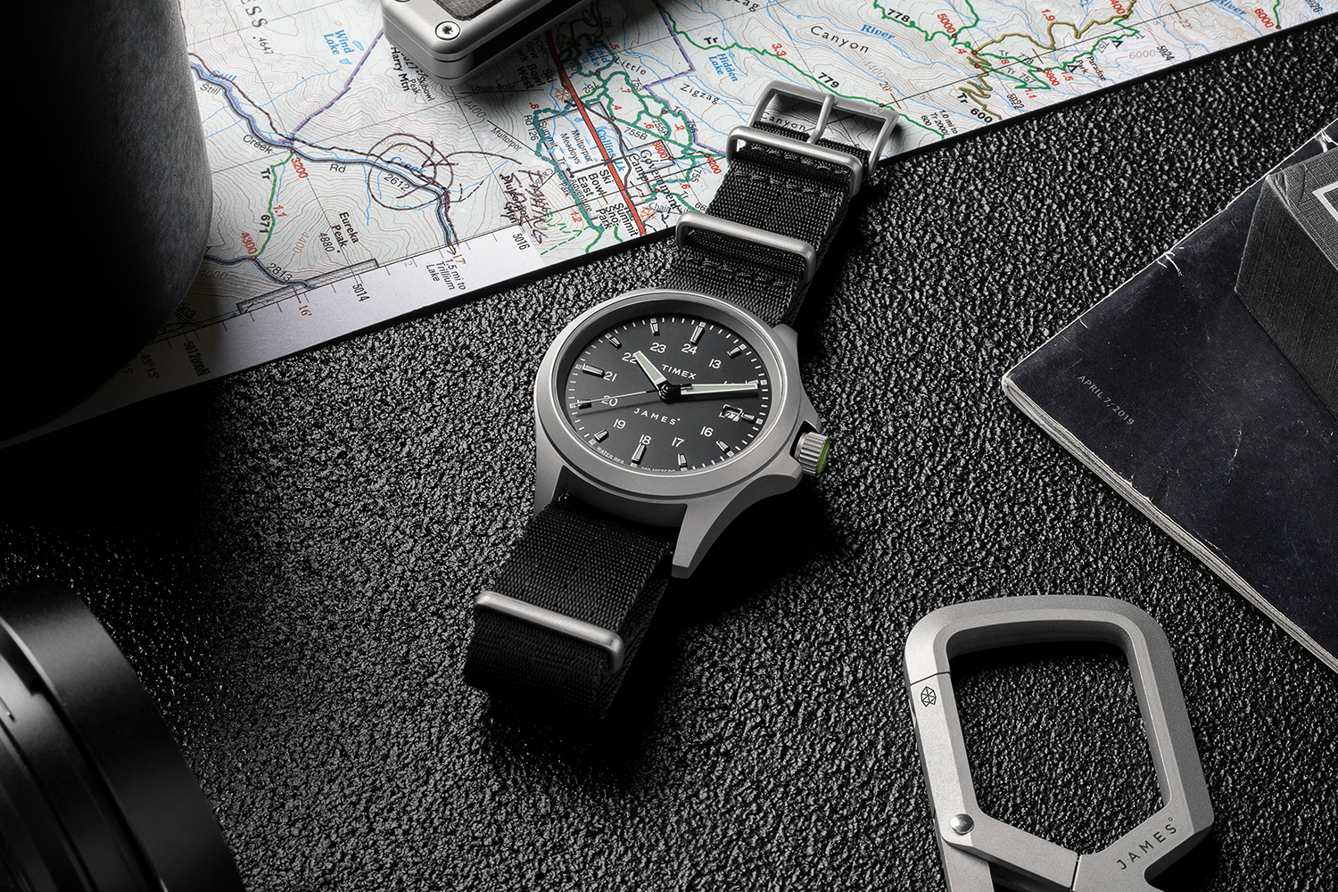 The new automatic watch from The James Brand and Timex lying on a table next to a map, pocketknife, keychain and coffee cup