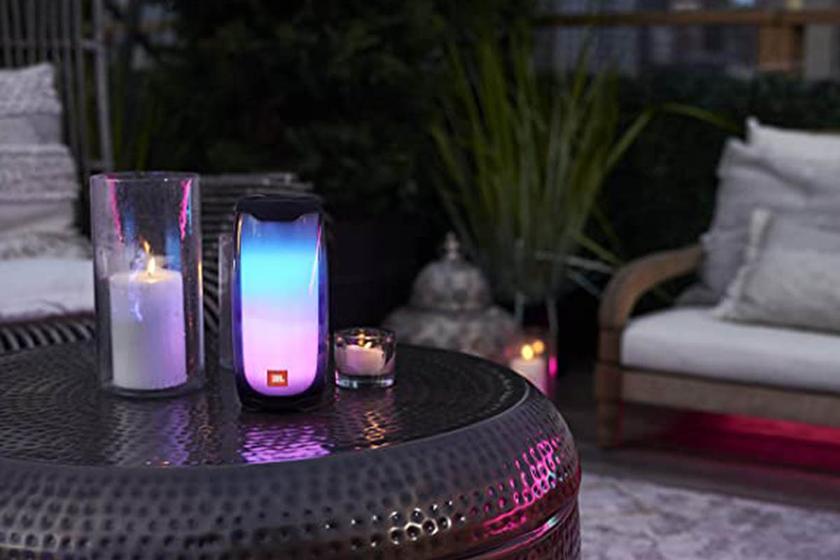 A lit-up JBL Pulse 4 speaker on an outdoor table at night. The speaker is currently on sale at Woot.