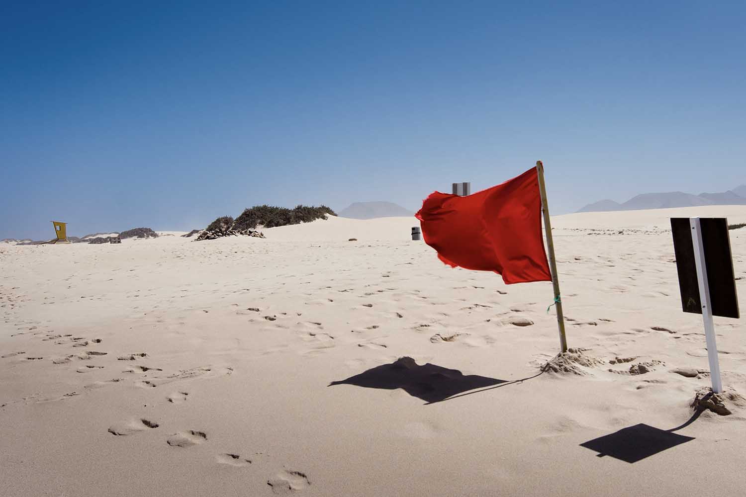 A red flag waving on a beach.