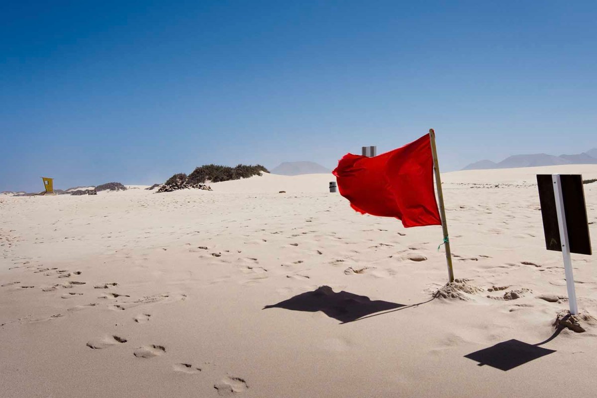 A red flag waving on a beach.