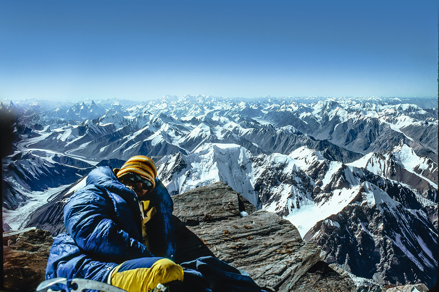 Rick Ridgeway on the summit of K2 in September 1978 huddled in a blue coat with a sea of snow-capped mountains in the background