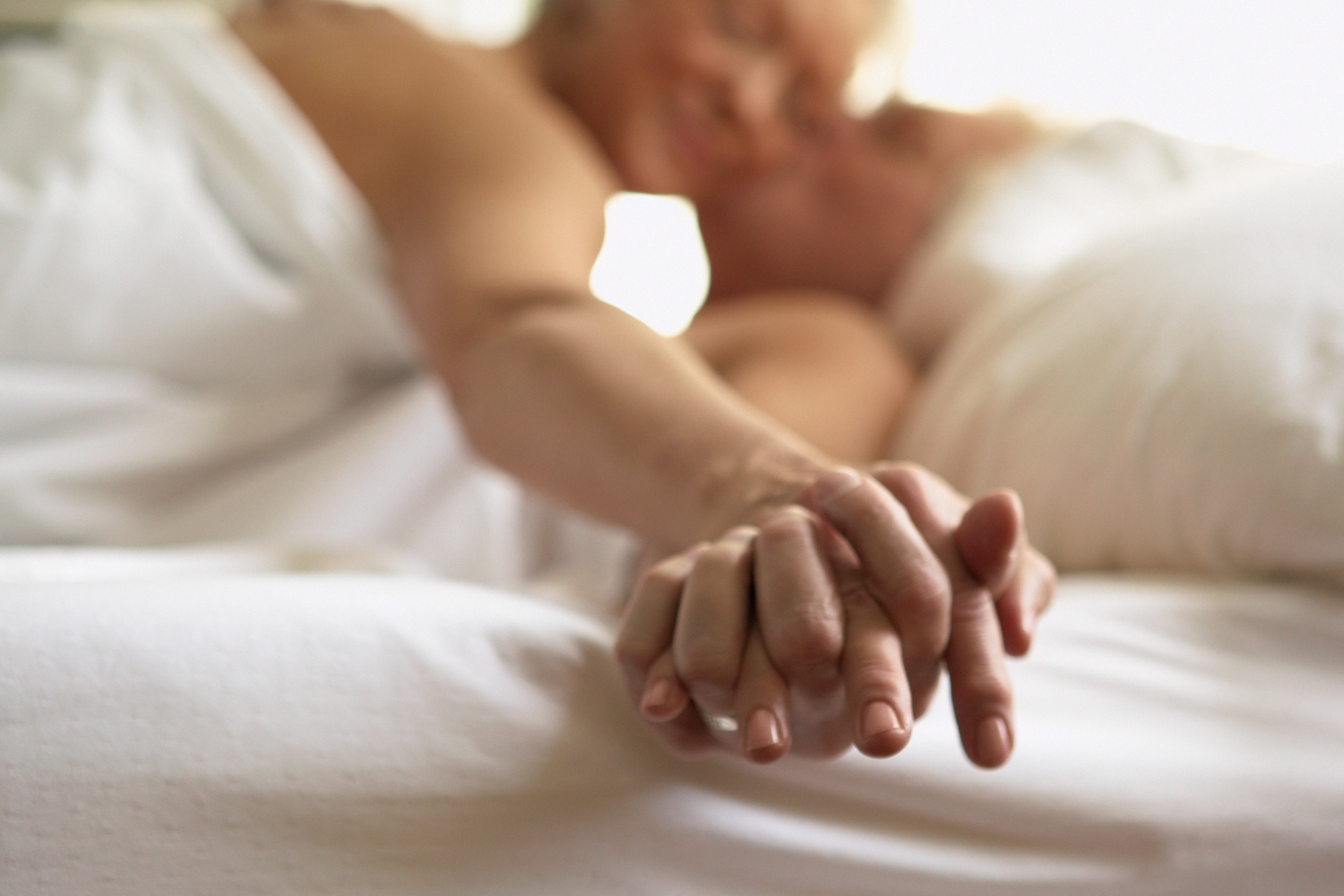 Photo shows an older couple lying in bed holding hands. According to recent studies, people over 50 are still having a lot of sex.