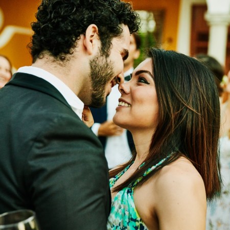 Smiling and embracing couple about to kiss during outdoor wedding reception. Tinder now offers a "plus one" service to bring dates to weddings.