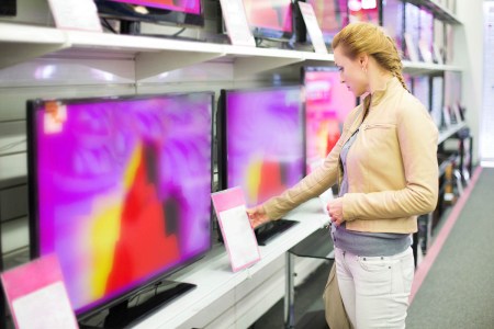 A woman looking at prices on TVs in a department store. TV prices have skyrocketed due to supply chain issues.