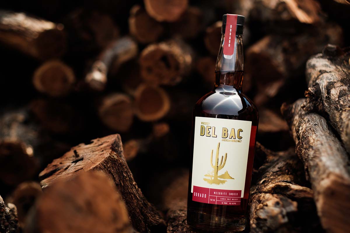 A bottle of Whiskey Del Bac sitting on mesquite wood