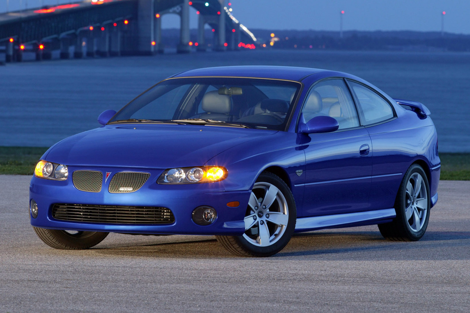 A 2004 Pontiac GTO in blue sitting in front of a bridge at twilight