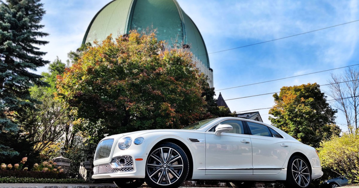 The 2022 Bentley Flying Spur sedan in white sitting in front of trees and a copper domed building