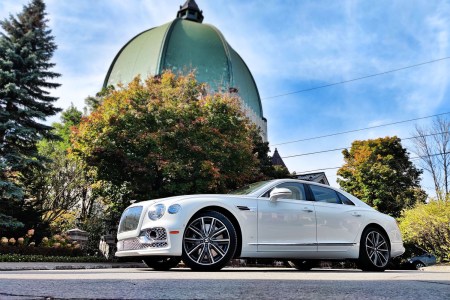 The 2022 Bentley Flying Spur sedan in white sitting in front of trees and a copper domed building