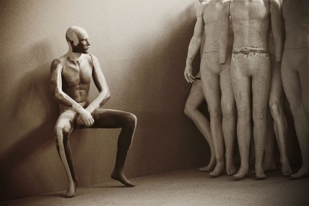 A nude mannequin sits gazing up at a group of other nude mannequins standing nearby