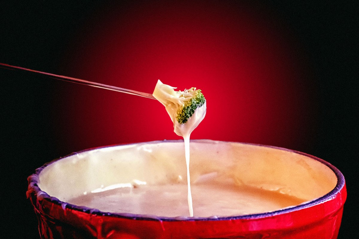 Speared broccoli dipped in cheese above a fondue pot
