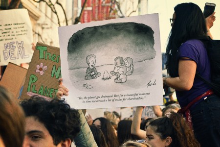 A protester at a climate march holding up a sign with Tom Toro's climate change cartoon from an issue of "The New Yorker" magazine from November 2012