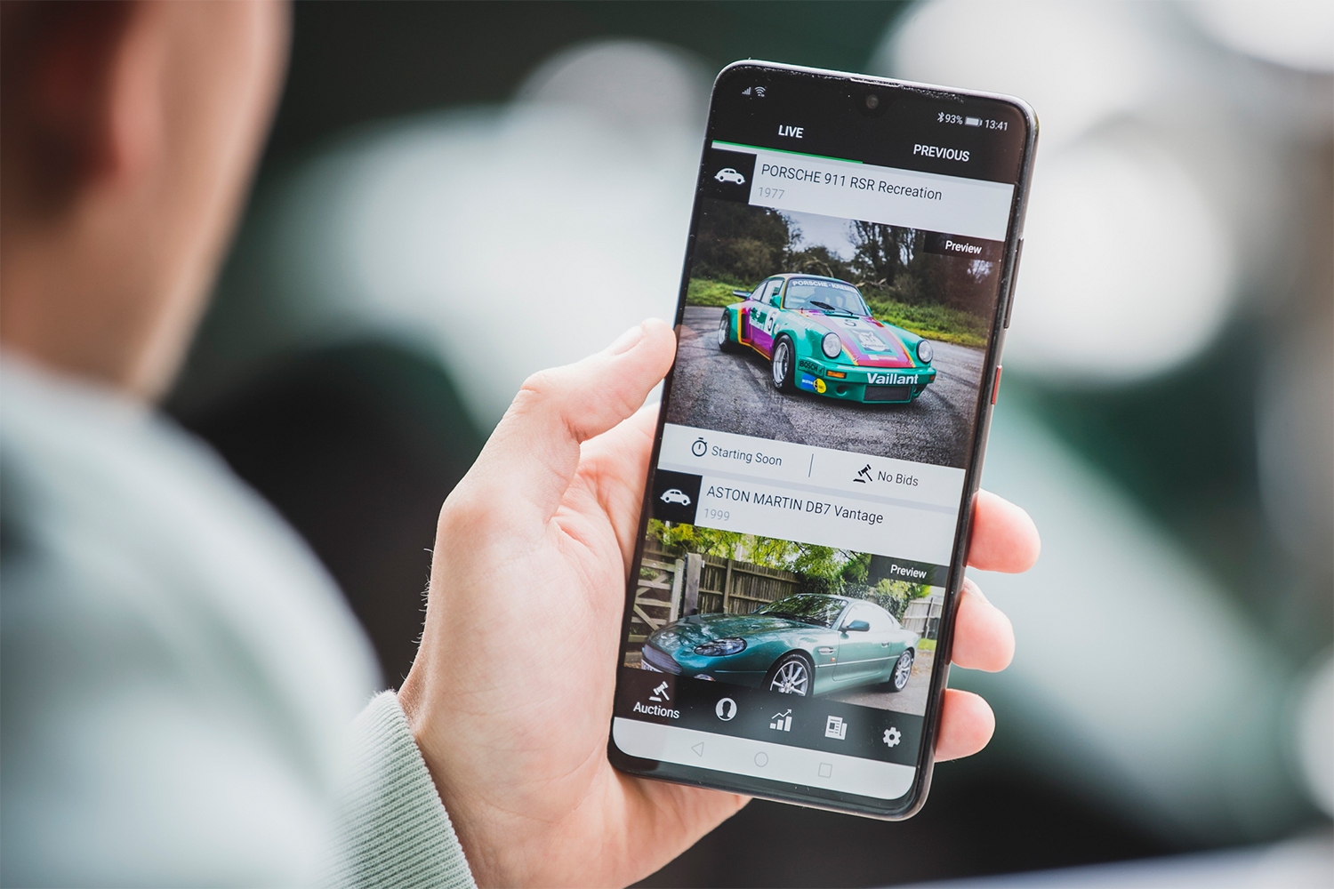 A man holding a smartphone showing the app for The Market by Bonhams, a new car auction site launching in the US in January 2022