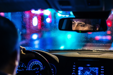 A driver in a car at night whose eyes can be seen in the rearview mirror