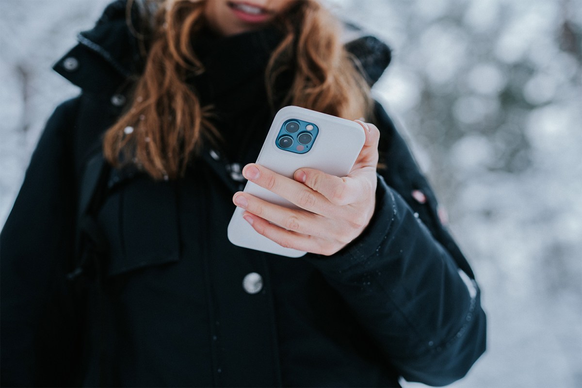 A woman holding an iPhone while standing outside in the snow while wearing a winter coat