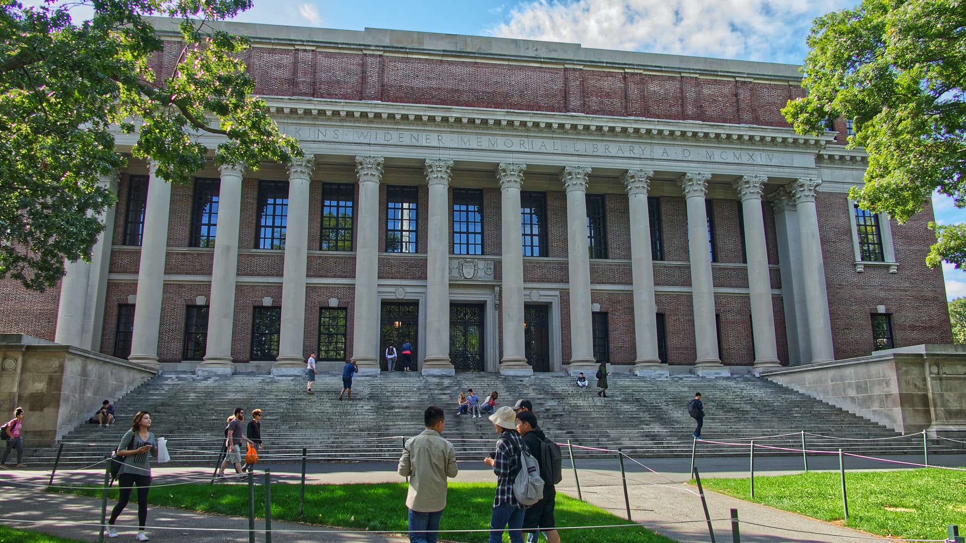 Students on the grass in front of and on the stairs of Widener Library at Harvard during the day