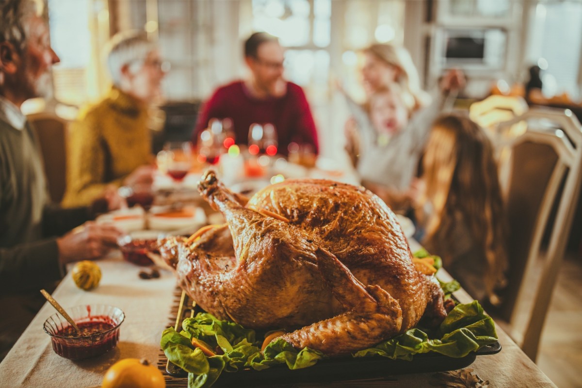 a thanksgiving turkey displayed on a dining room table, blurred family around table in background